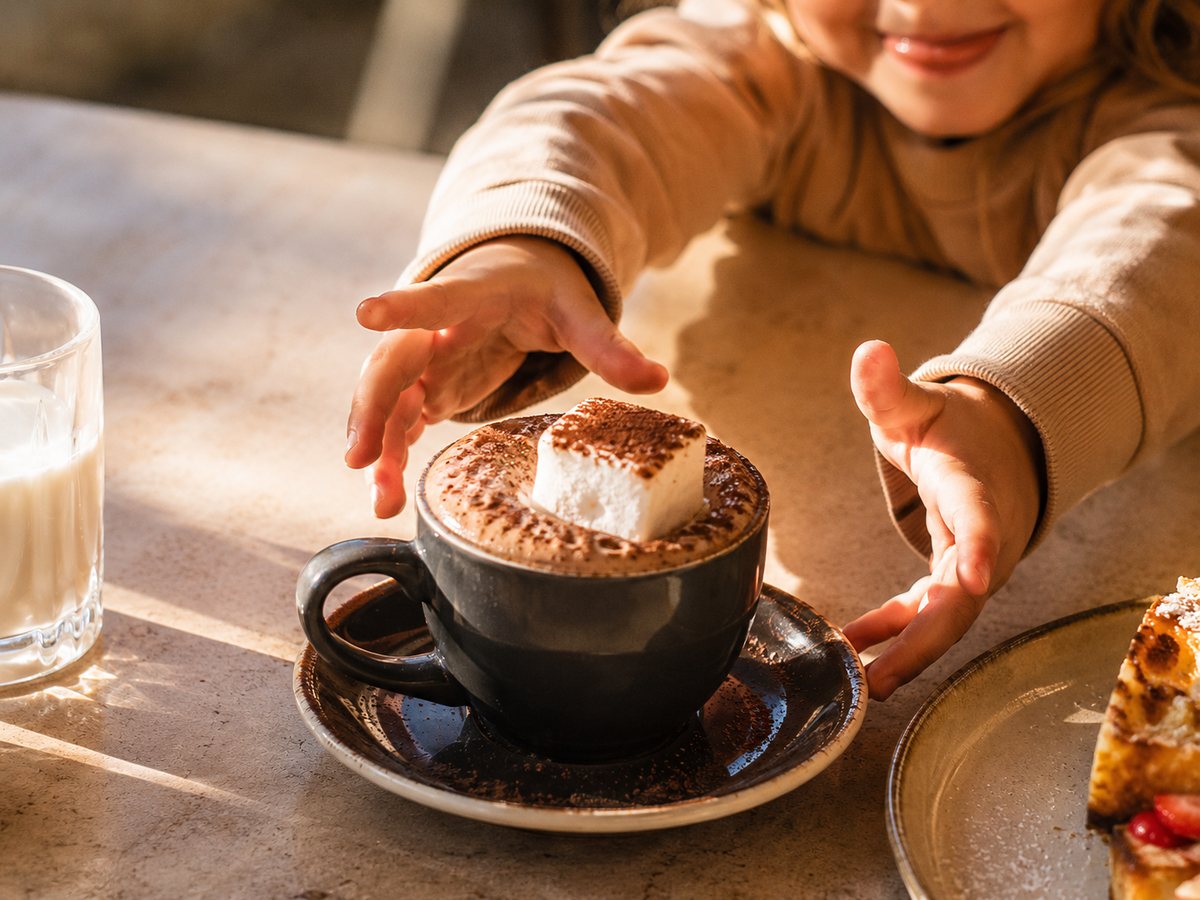 A babycino with marshmallow, tiny hands reaching for it.